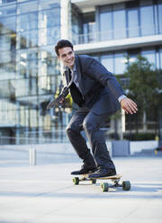 Smiling businessman skateboarding outside urban building - CAIF28478