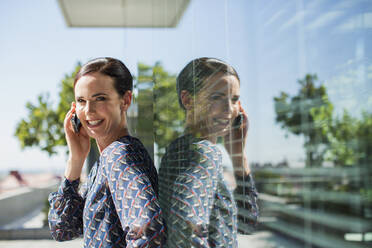 Lächelnde Geschäftsfrau, die im Freien mit einem Handy telefoniert - CAIF28485