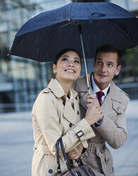 Geschäftsmann und Geschäftsfrau beobachten Regen unter Regenschirm - CAIF28489