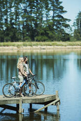 Couple with bicycles on dock overlooking lake - CAIF28492