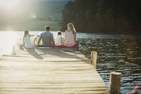 Family sitting at the edge of dock over lake - CAIF28502