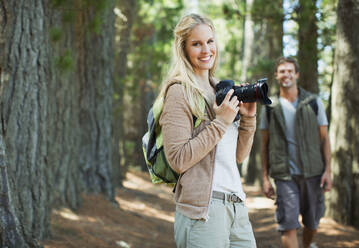 Smiling woman with digital camera in woods - CAIF28503