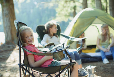 Lächelndes Mädchen auf einem Stuhl auf dem Campingplatz - CAIF28506