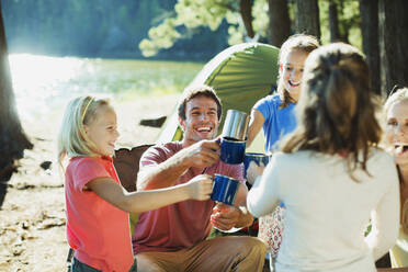Lächelnde Familie stößt auf dem Campingplatz mit Tassen an - CAIF28513
