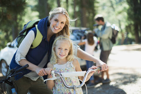 Smiling mother and daughter with bicycle in woods stock photo