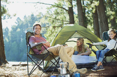 Lächelnde Familie entspannt sich auf einem Campingplatz im Wald - CAIF28517