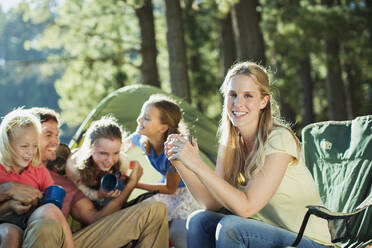 Lächelnde Familie entspannt sich auf einem Campingplatz im Wald - CAIF28519