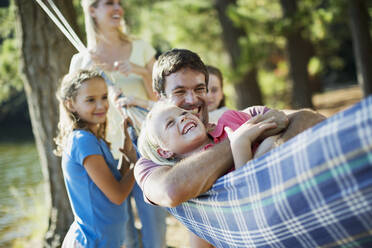 Happy family laying in hammock in woods - CAIF28522