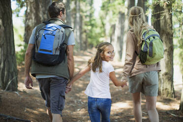 Smiling girl hiking with parents in woods - CAIF28549