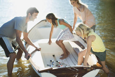 Family getting into rowboat with fishing rods on lake - CAIF28554