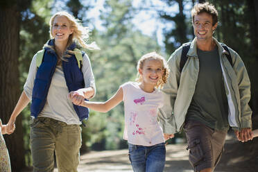 Smiling family holding hands and running in woods - CAIF28559