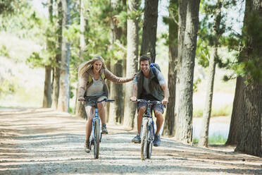 Smiling couple mountain biking in woods - CAIF28562