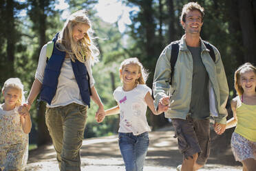 Smiling family holding hands and walking in woods - CAIF28567