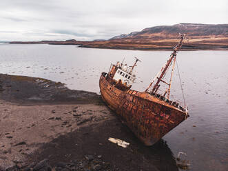 Old rusty fishing boat moored on beach in foggy morning in