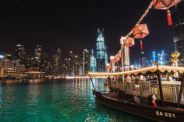 Lovely boat and crowded pier near rippling water at amazing night in brightly illuminated city of Dubai - ADSF06183