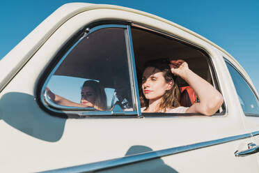 Freundinnen sitzen im Retro-Auto und fahren in der Natur mit hellem Sonnenlicht reisen zusammen in der Sommerzeit - ADSF06197