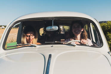 Gruppe glücklicher multiethnischer Frauen im Auto, die im hellen Sonnenlicht zusammen fahren und lachen - ADSF06198