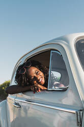 Glückliche junge schwarze Frau mit modischer Sonnenbrille, die aus dem Autofenster schaut und die Sommersonne genießt - ADSF06208