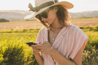 Brünette in rosa Kleidung und eleganten Hut Surfen Smartphone auf dem Hintergrund der grünen Sommerlandschaft in? - ADSF06220