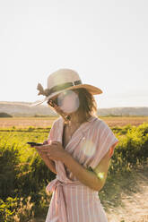 Brünette in rosa Kleidung und eleganten Hut Surfen Smartphone auf dem Hintergrund der grünen Sommerlandschaft in? - ADSF06221
