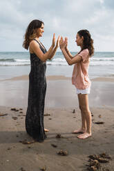 Seitenansicht einer lächelnden Mutter mit einer in den Händen spielenden Tochter am sommerlichen Meeresstrand - ADSF06250