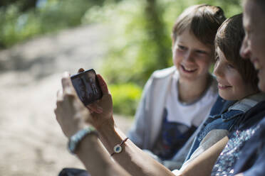 Mutter und Söhne unterhalten sich im Park per Videochat mit Freunden auf dem Smartphone - CAIF28581