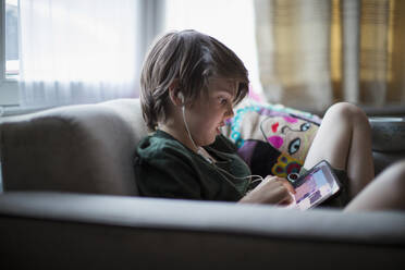 Junge mit Kopfhörern und digitalem Tablet im Wohnzimmer - CAIF28587