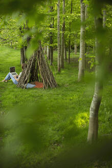 Woman using laptop at branch teepee in woodland - CAIF28617