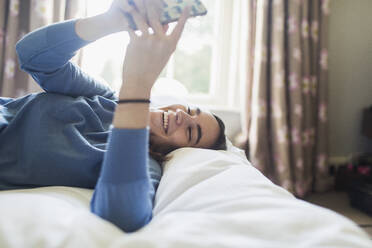 Glückliches Teenager-Mädchen mit Smartphone auf dem Bett - CAIF28622