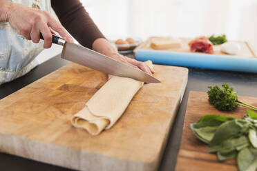 Woman cutting fresh homemade pasta on cutting board - CAIF28640