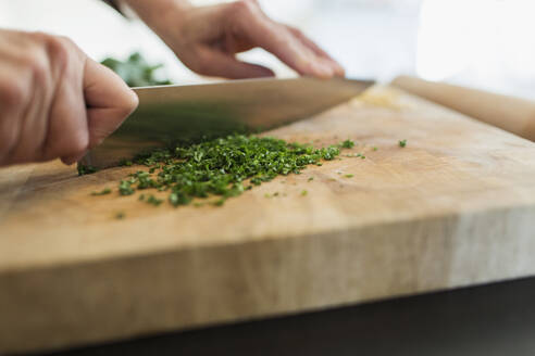 Close up woman cutting fresh herbs with knife on cutting board - CAIF28650