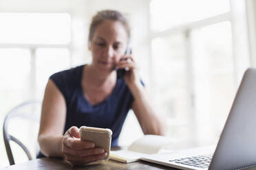 Woman talking on telephone and using smart phone at home - CAIF28654