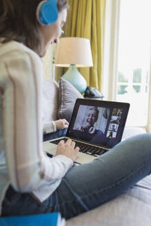 Teenage girl with headphones and laptop video chatting with friends - CAIF28711