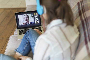 Teenage girl with laptop video chatting with friends on sofa - CAIF28715