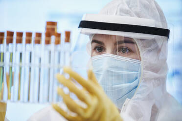 Wissenschaftlerin in sauberem Anzug bei der Untersuchung von Reagenzgläsern - CAIF28730