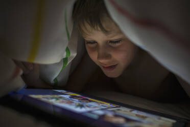 Close up boy using digital tablet under blanket - CAIF28793