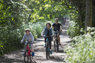 Mother and sons bike riding on sunny park path - CAIF28798