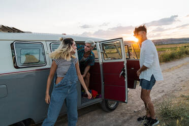 Junge Männer und Frau, die aus einem Retro-Van aussteigen, während sie gemeinsam durch die schöne Natur reisen - ADSF06299