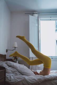 Side view of young woman with bare breasts wearing yellow tights and  keeping legs in air