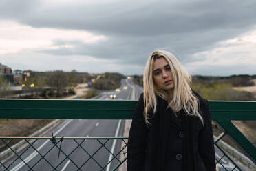 Pretty blonde woman standing at fence on bridge over the road. - ADSF06350