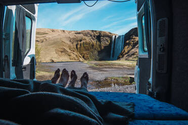 Mit einer Decke bedeckte Beine eines Mannes und einer Frau im Campingwagen in der Nähe eines Wasserfalls - ADSF06357