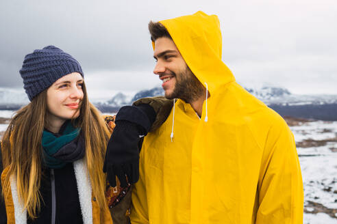 Content man and woman standing together and smiling on background of cold mountains of Iceland. - ADSF06376