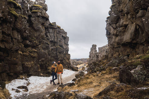 Ein reisendes Paar, das auf einem schmalen Pfad zwischen schneebedeckten Felsen an einem düsteren Tag steht, Island. - ADSF06377