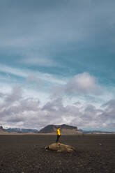 Anonymous man standing on rock among rocky plain with mountains behind under cloudy sky, Iceland. - ADSF06394