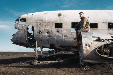 Mann sitzt auf altem, zerstörtem Flugzeug - ADSF06403