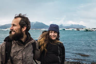 Bärtiger Mann und lachendes Mädchen in warmer Kleidung vor dem Hintergrund des kalten isländischen Meeres. - ADSF06409