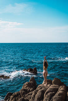 Seitenansicht einer nackten Frau, die sich mit den Händen auf einem Felsen am Meer streckt. - ADSF06452