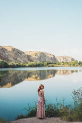 Woman in long summer dress on lake shore - ADSF06468