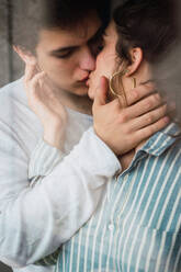 View through window of young man and woman in pajamas standing and kissing with tender. - ADSF06485