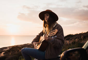 Woman sitting on car and playing guitar - ADSF06509